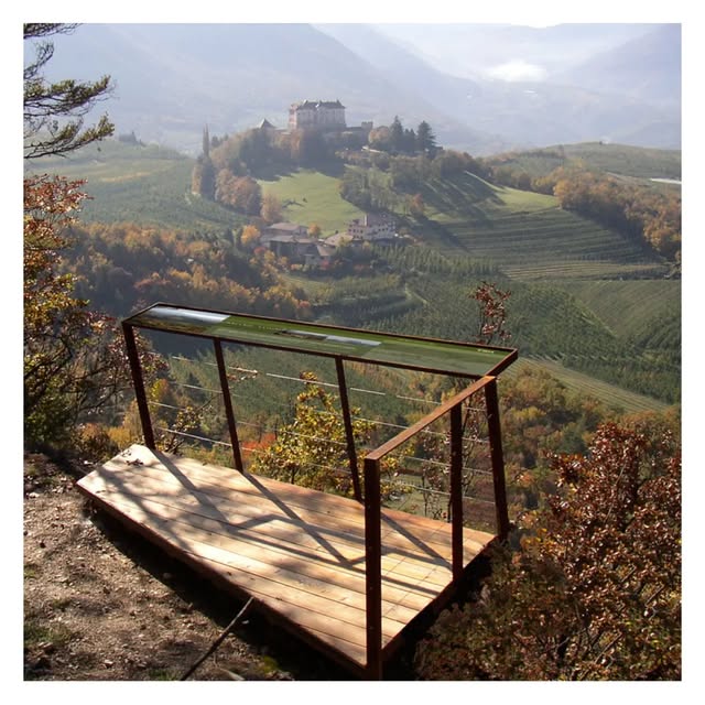 Belvedere in legno e acciaio affacciato su un versante a vigneto con un castello sul poggio di fronte