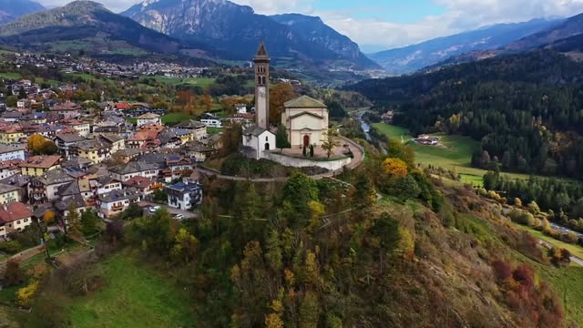 Veduta aerea di un borgo di montagna con la chiesa sul promontorio e le pareti dolomitiche sullo sfondo